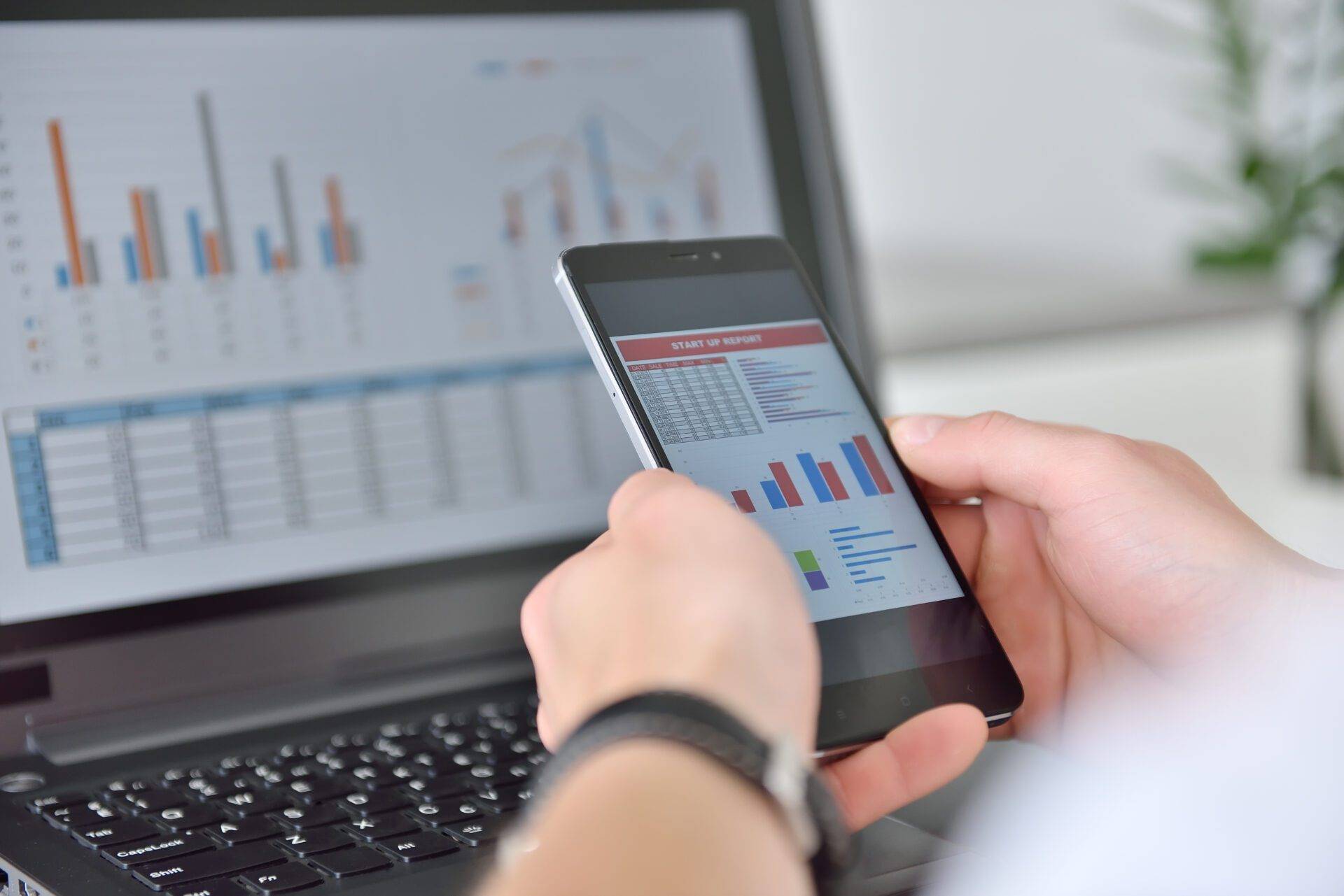 Person som granskar diagram och rapporter på både mobiltelefon och laptop.
